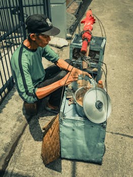 A street vendor preparing traditional food with cooking equipment on a sunny day.