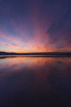 Stunning sunset with vivid colors reflecting on calm water, creating a serene and peaceful scene.
