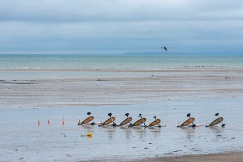 Free A row of kite buggies parked on a vast beach during low tide under cloudy skies. Stock Photo