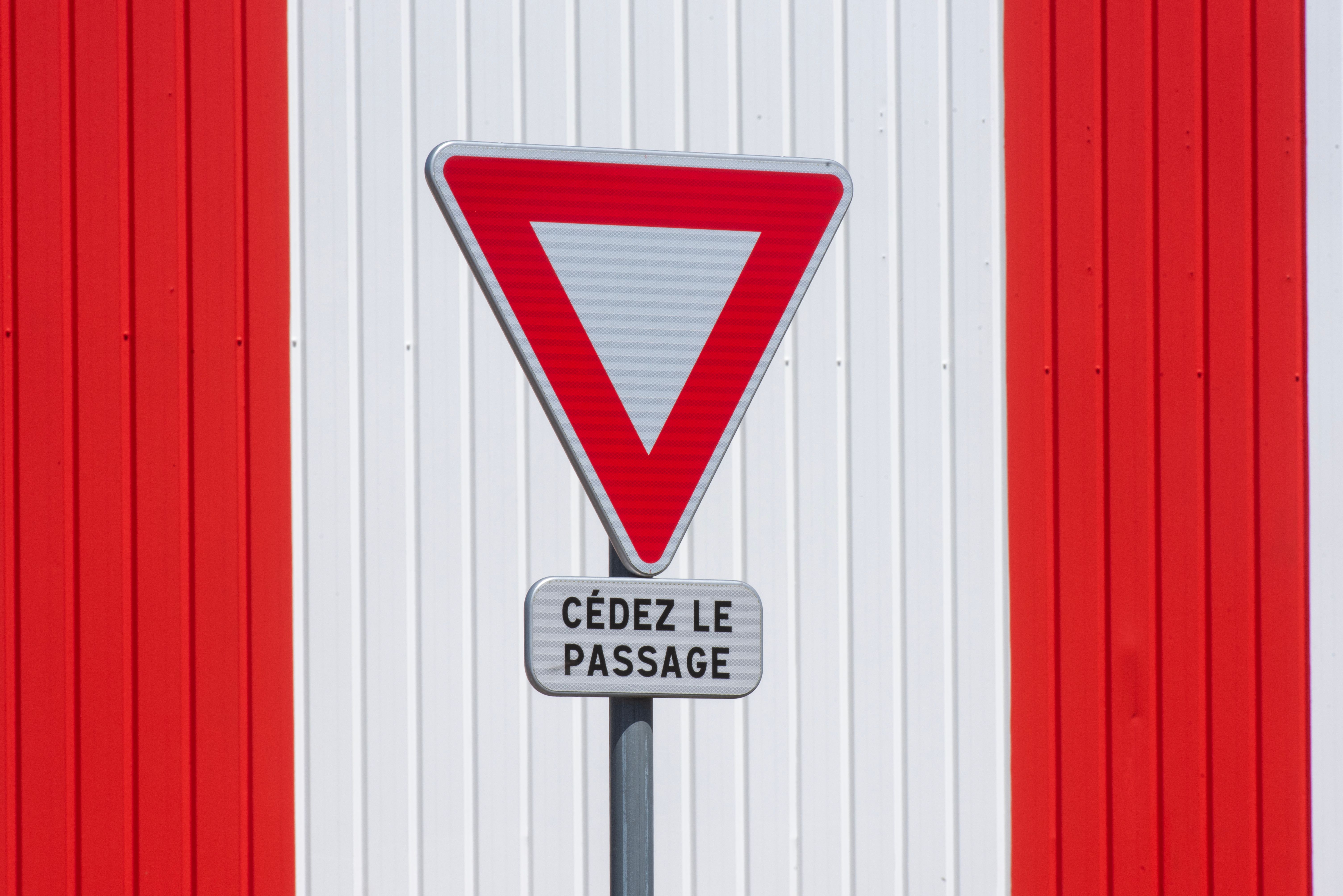 Yield Sign Against Red and White Striped Wall · Free Stock Photo