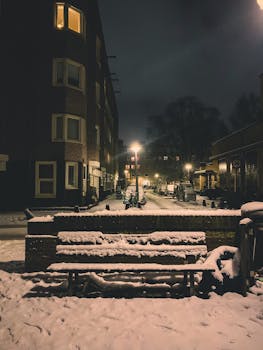 Idyllic Amsterdam street at night covered in snow, illuminated by streetlights.
