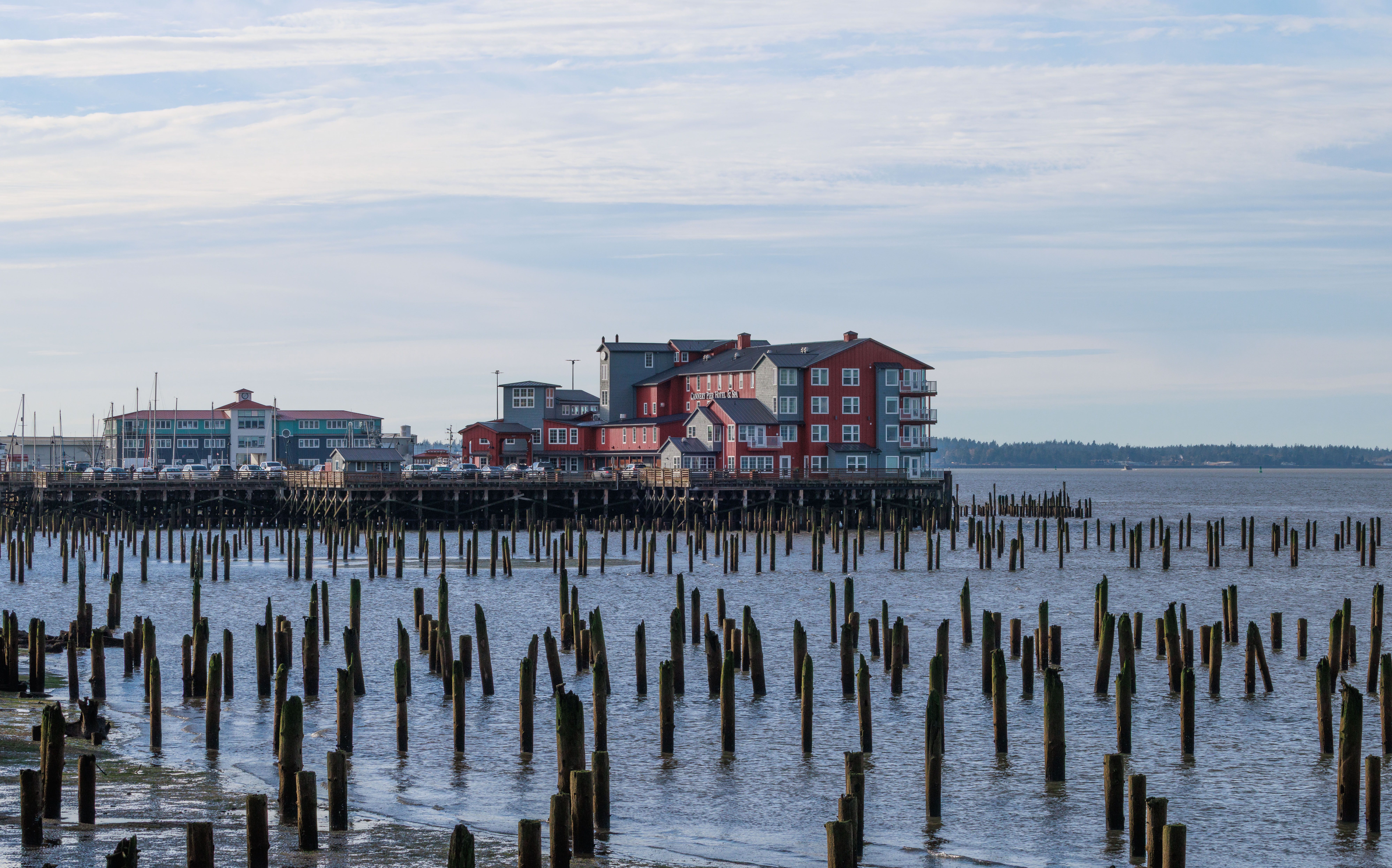 Red buildings on a coastal pier surrounded by wooden pilings in a serene marine setting.