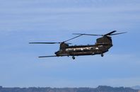 A Chinook helicopter flying over a scenic landscape with a clear blue sky.