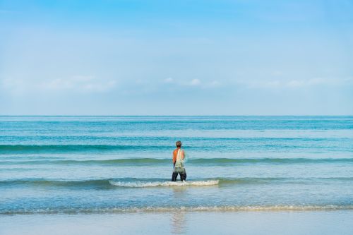 Free A lone man standing in the ocean waves, embracing the serene seascape. Stock Photo