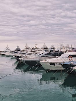 A row of luxurious yachts docked at a serene marina under a cloudy sky.