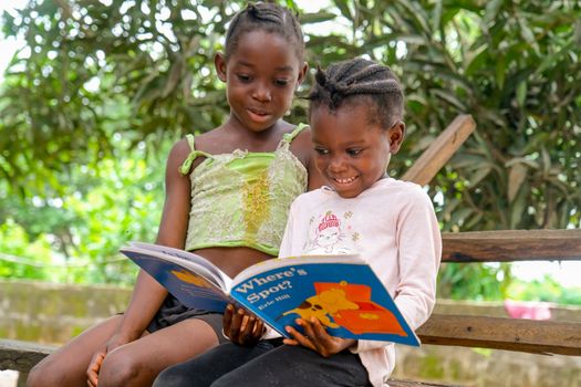 Two children enjoying a storybook outdoors, sharing a joyful reading moment.