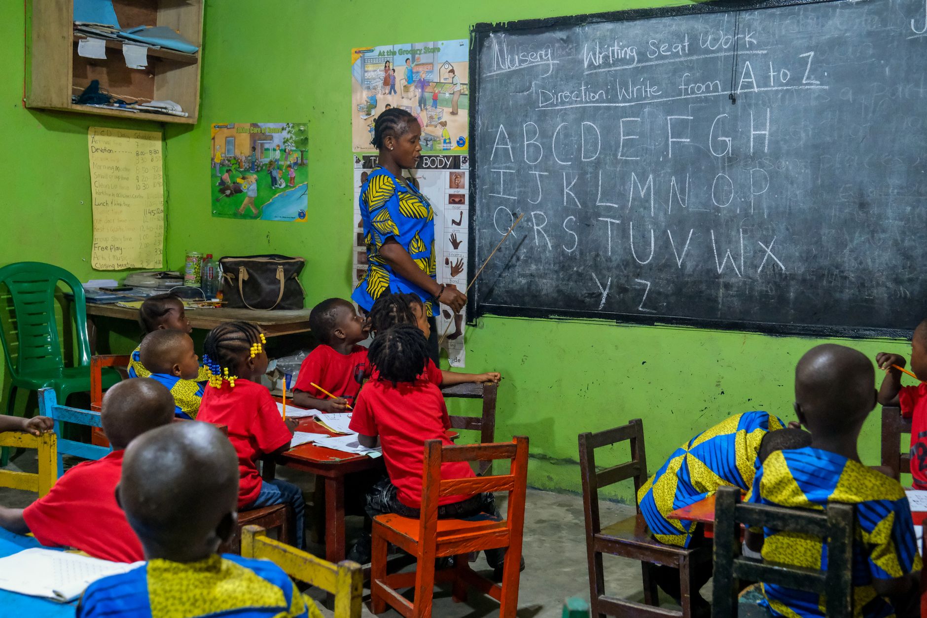 Young students learn the alphabet with a teacher in a vibrant Liberian classroom setting.