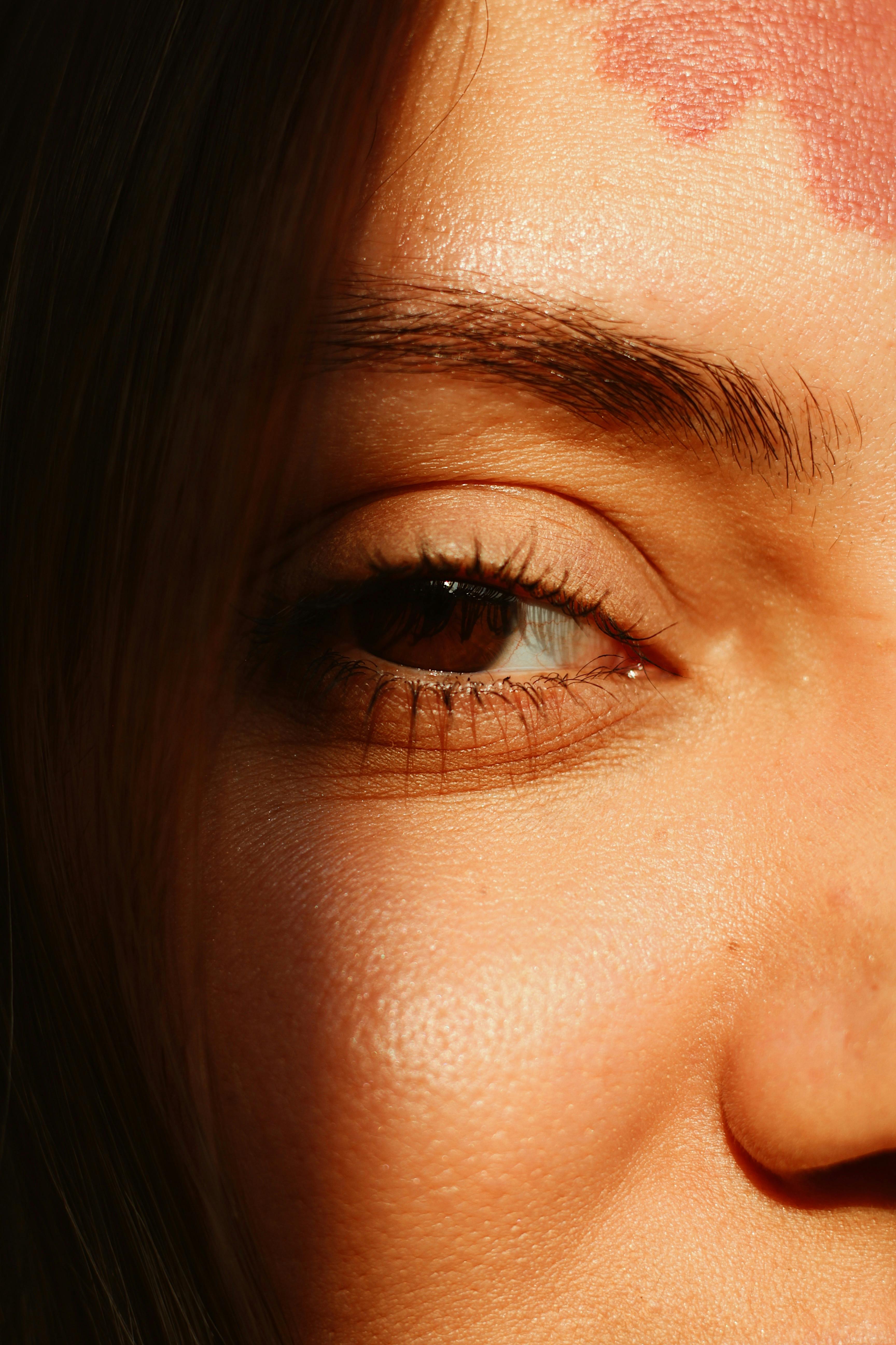 Close-up shot highlighting a woman's eye with a heart symbol on the forehead in natural light.
