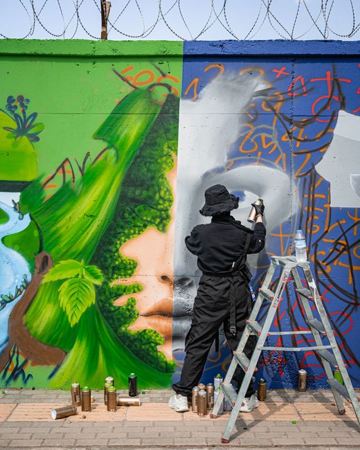 A street artist in black outfit painting a vivid mural on a city wall.