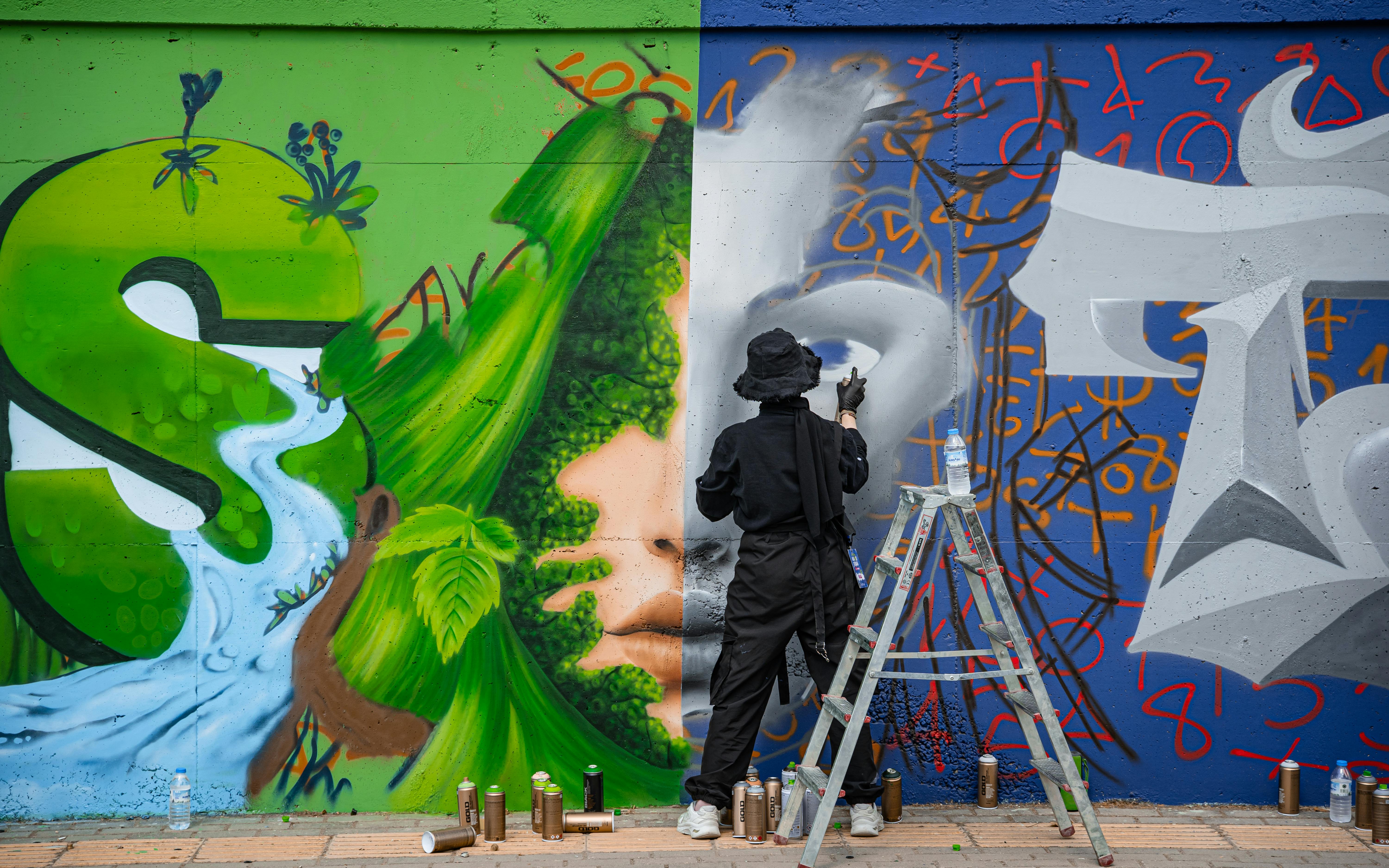 Artist painting a vivid mural featuring nature and abstract designs on an urban wall.