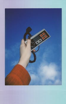 A retro game controller held up against a vibrant blue sky, exuding nostalgia and tech culture.