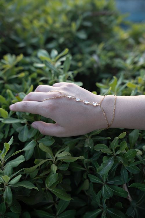 Free Close-up of a woman's hand adorned with delicate gold jewelry in a natural outdoor setting. Stock Photo