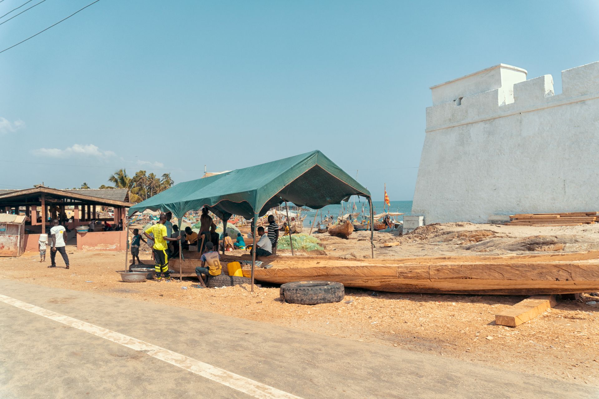 Market scene under a green tent near Elmina Castle, Ghana. People gathered by the seaside.