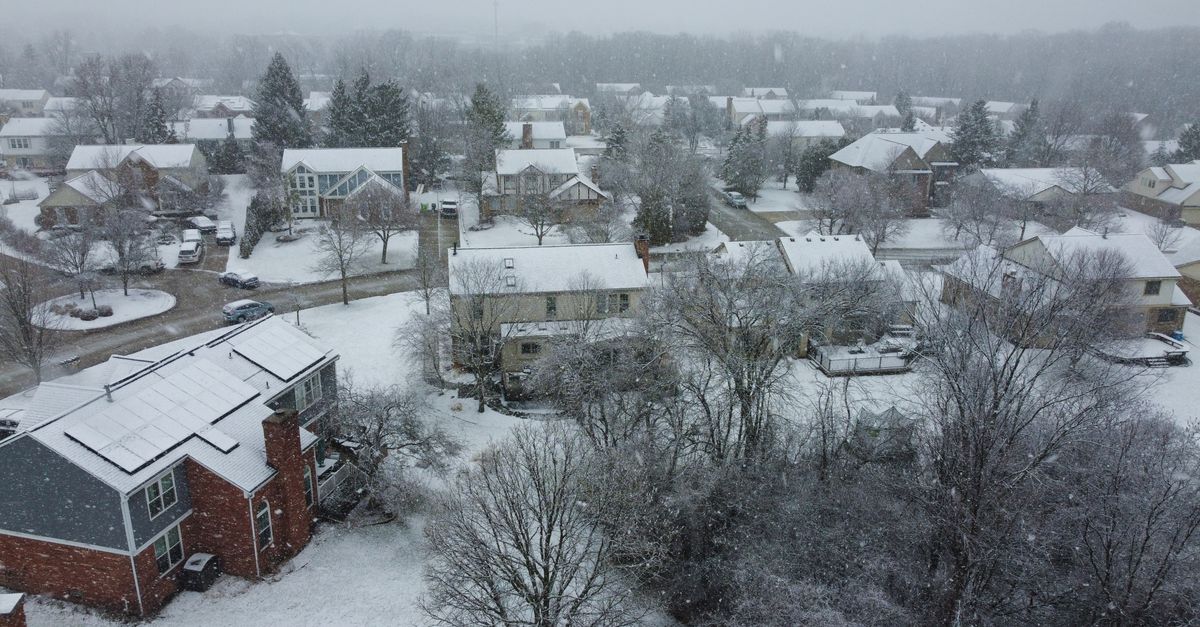 Aerial shot of a suburban neighborhood covered in snow during winter, creating a serene winter landscape.