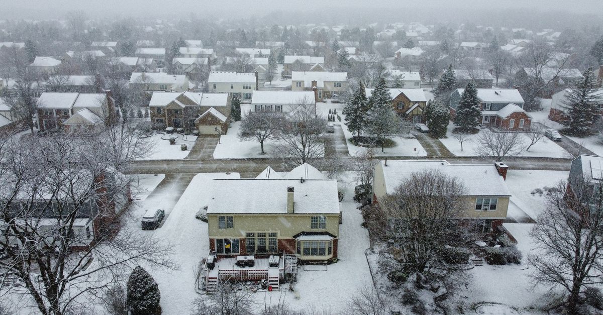 Snow-covered suburban neighborhood with houses and trees in a scenic winter landscape.