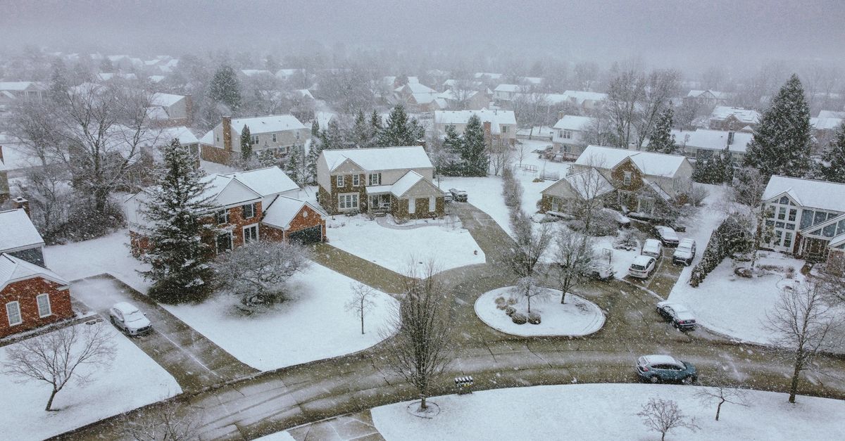 Aerial shot of a suburban neighborhood blanketed in snow during a calm winter day.
