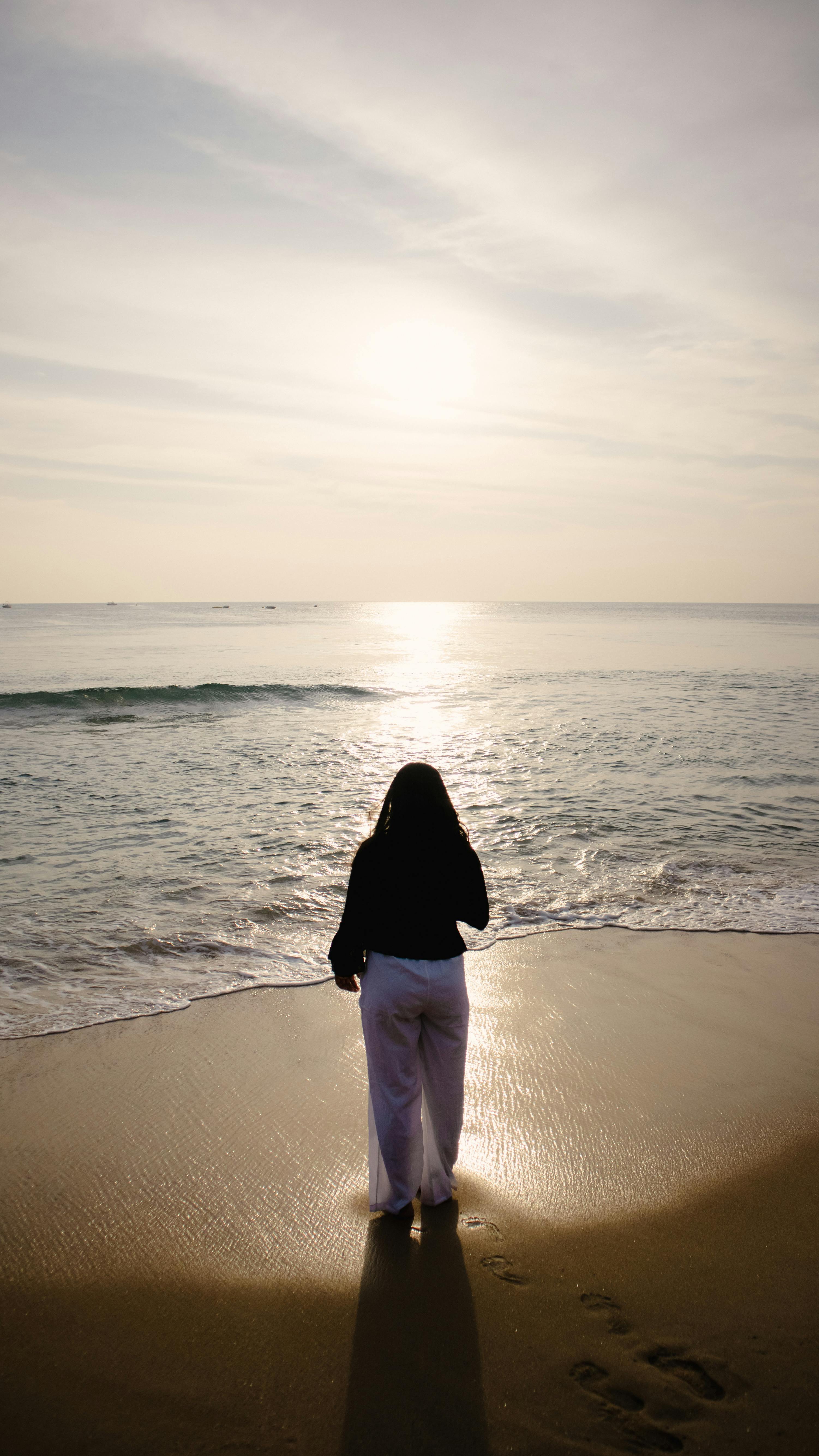 A lone walker at sunrise on a beach, suggesting solitude without pretending recovery.