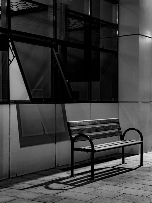 Free A solitary bench set against a city building in monochrome night lighting. Stock Photo