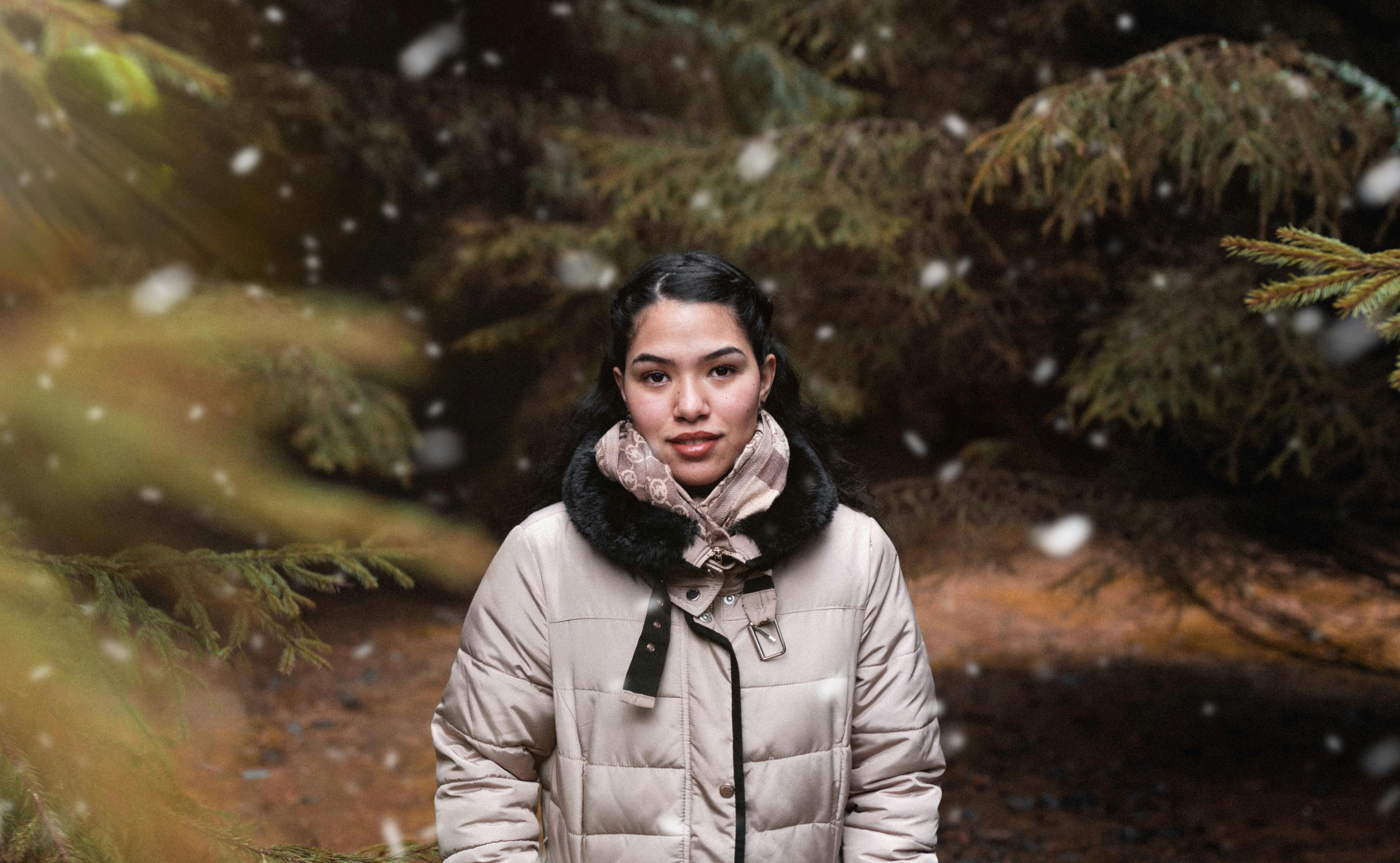 一个穿着冬衣的女人肖像，在户外雪花飘落、树木环绕的环境中