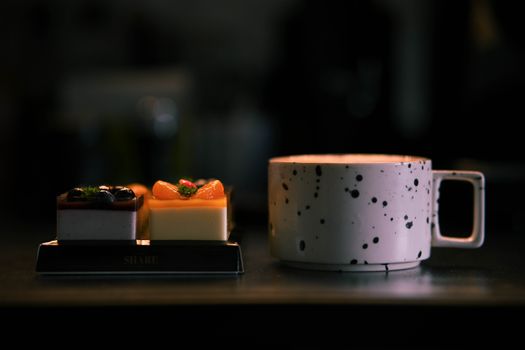 Stylish speckled coffee mug alongside gourmet desserts in dimly lit setting.