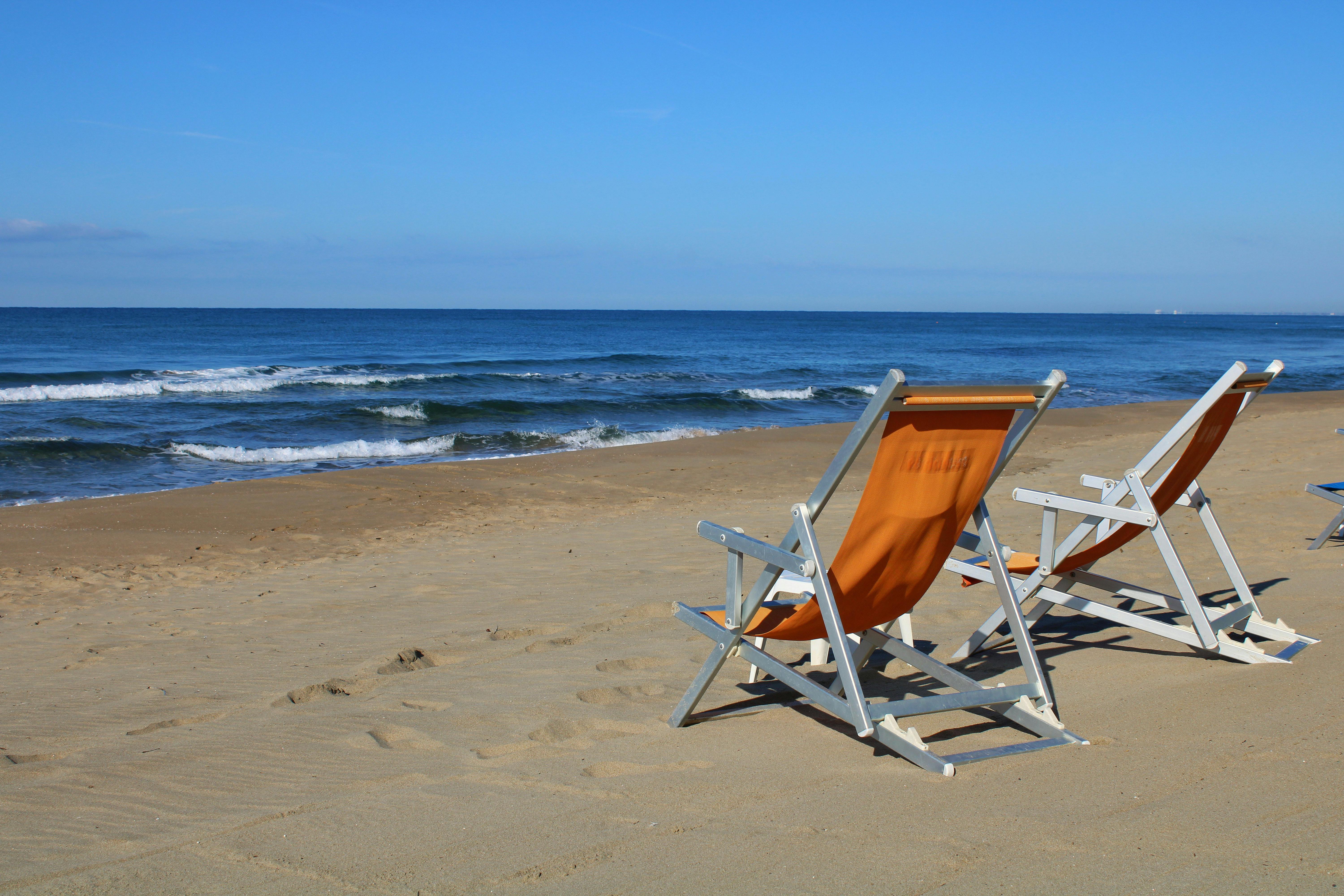 Two empty deck chairs on a sandy beach under clear blue skies in Latina, Italy.