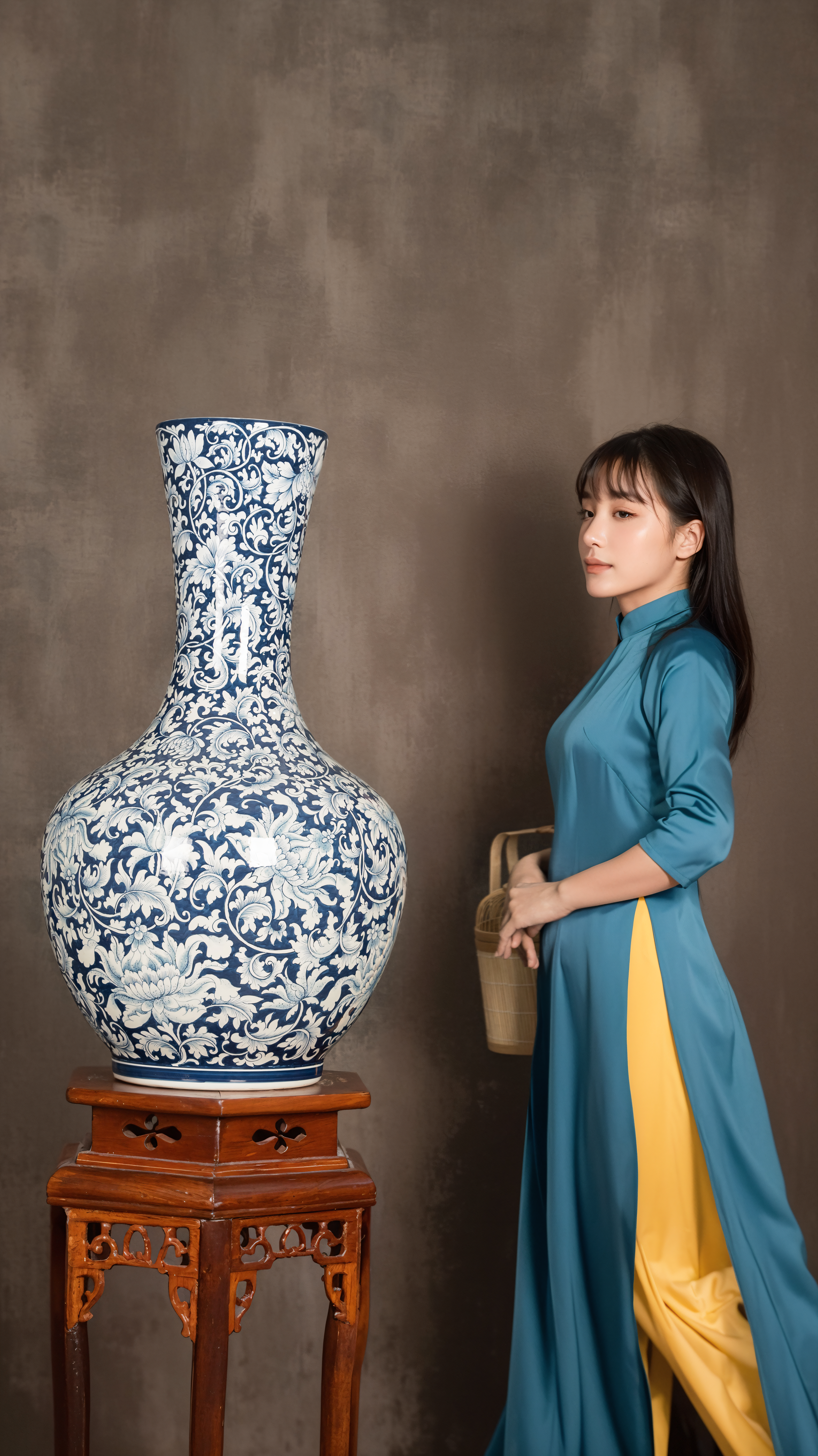 A woman in a traditional Ao Dai stands beside a detailed blue and white vase, exuding elegance and style.