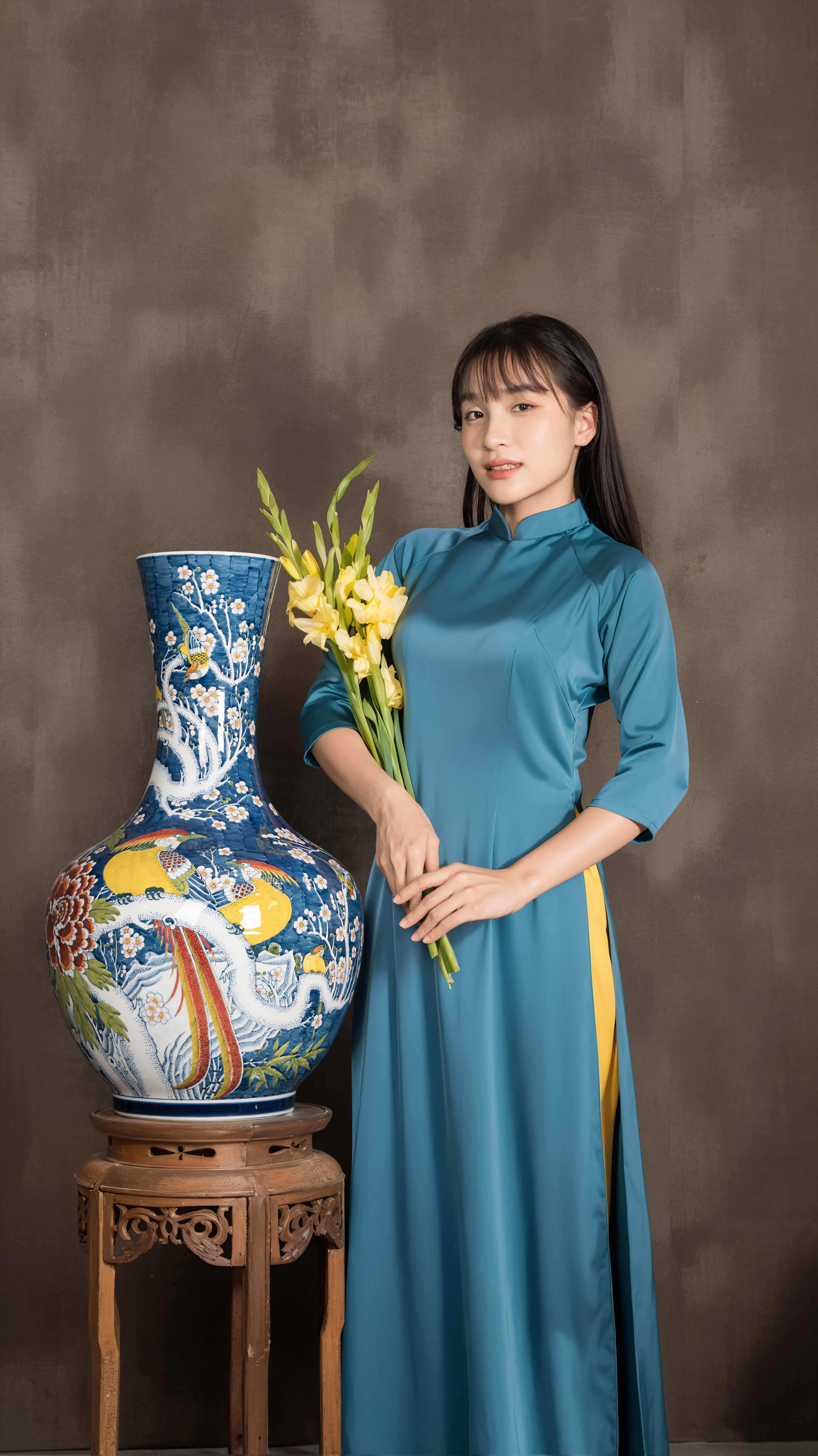 A woman in a teal traditional dress stands with a decorative vase and flowers.