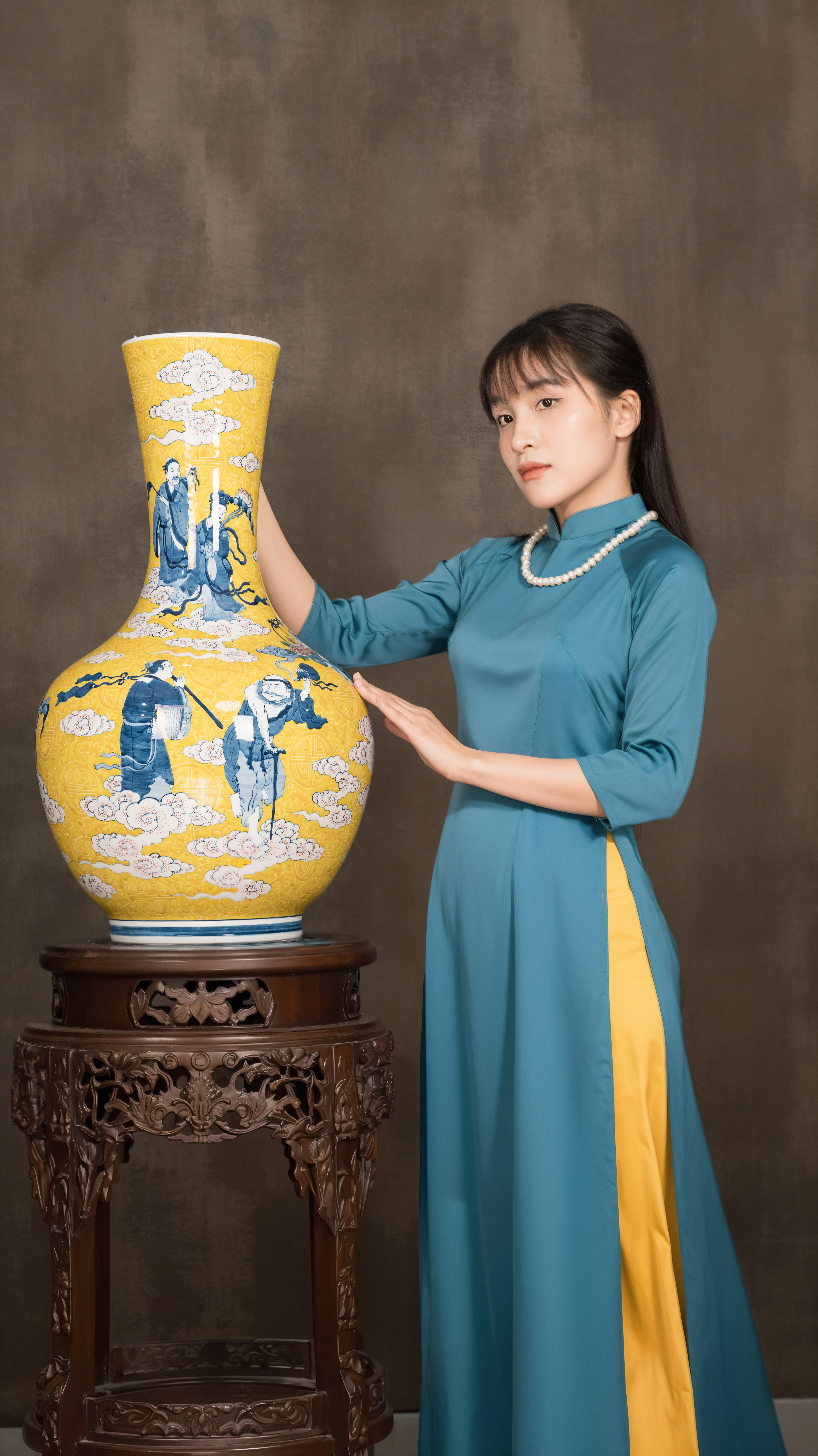 A woman in traditional attire poses with a decorative Chinese vase indoors.