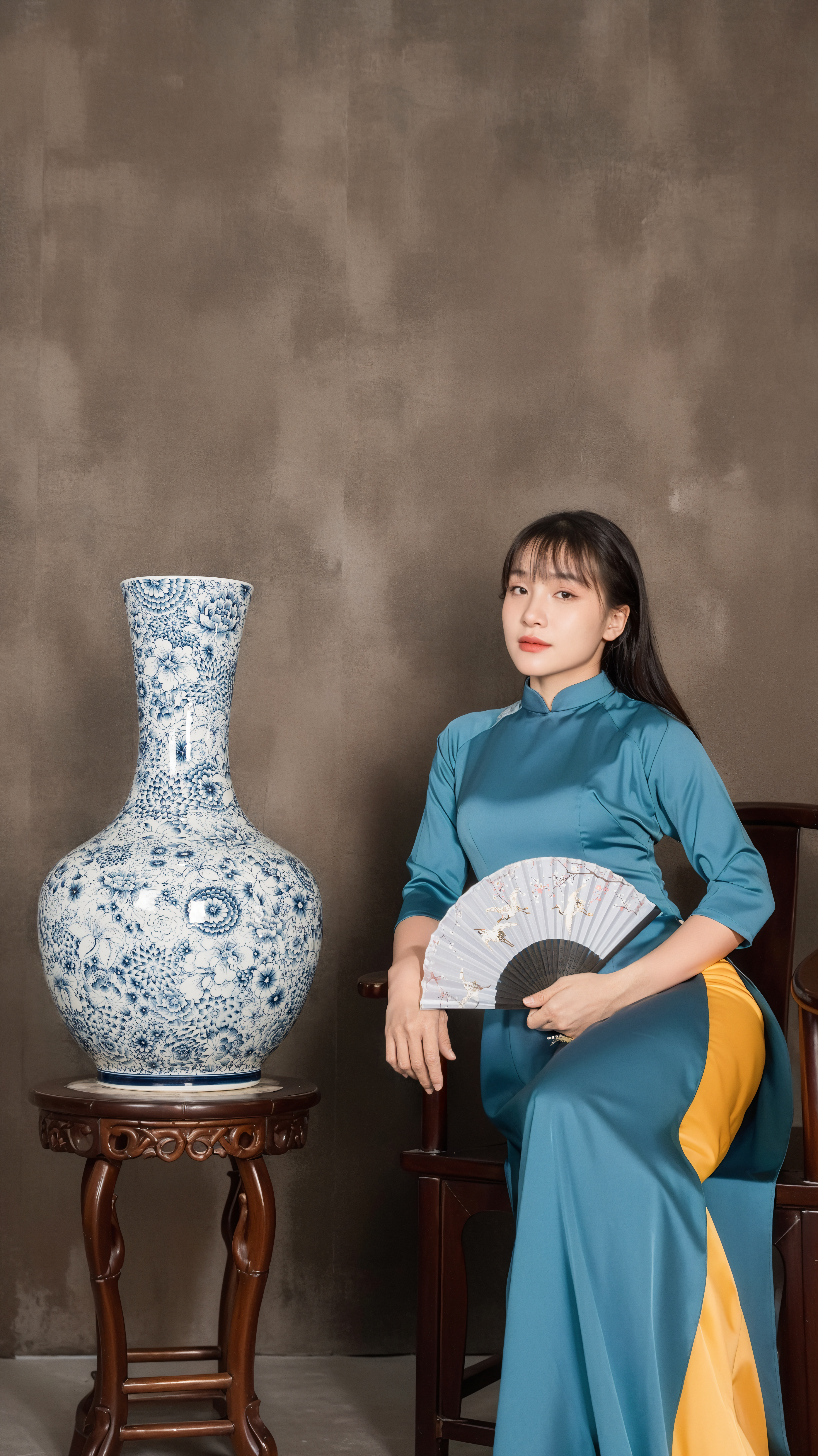 A woman in traditional attire sits indoors with a decorative vase, embodying cultural elegance.