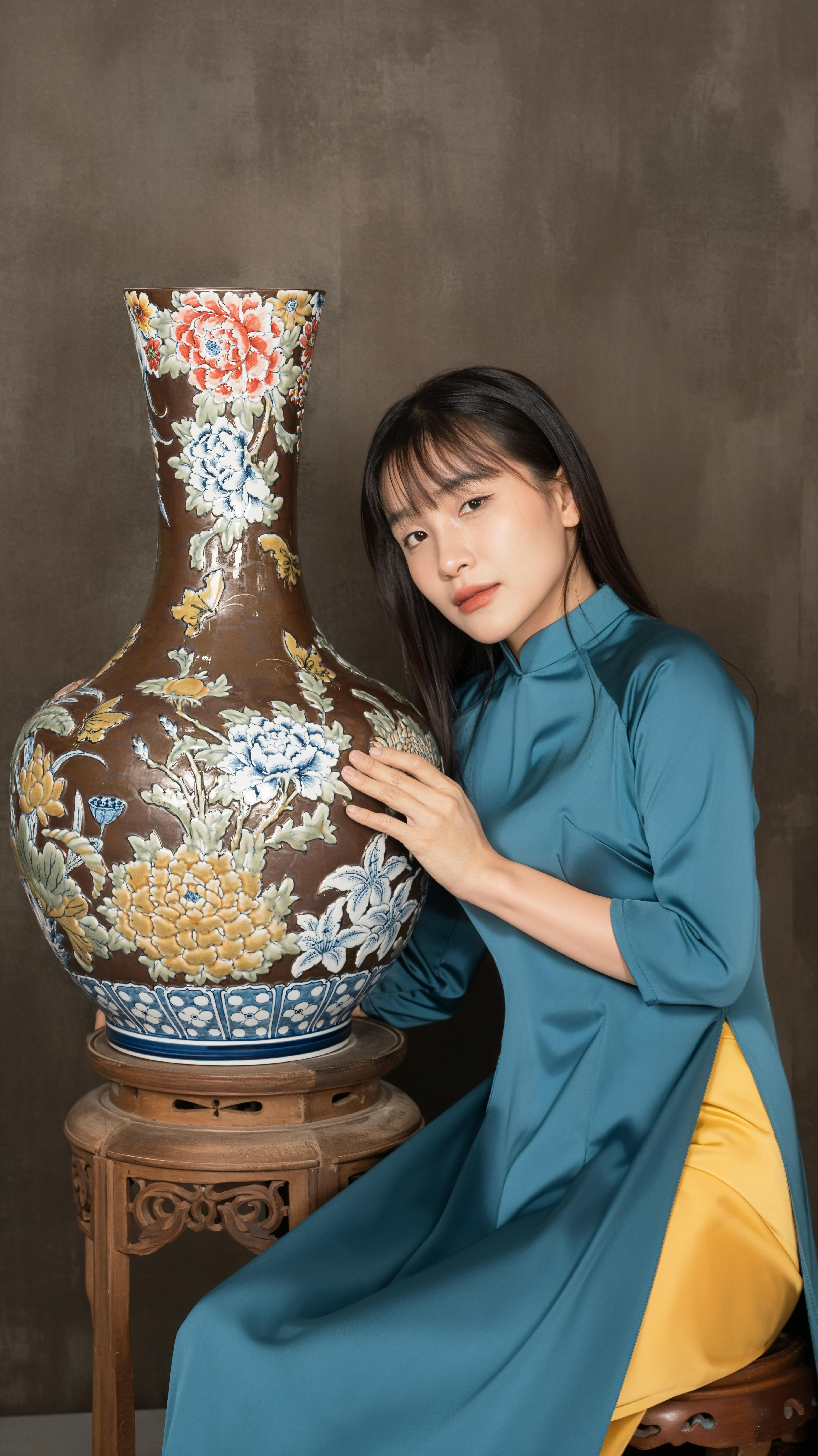 Woman in traditional attire poses with a large, ornate enamel vase indoors.