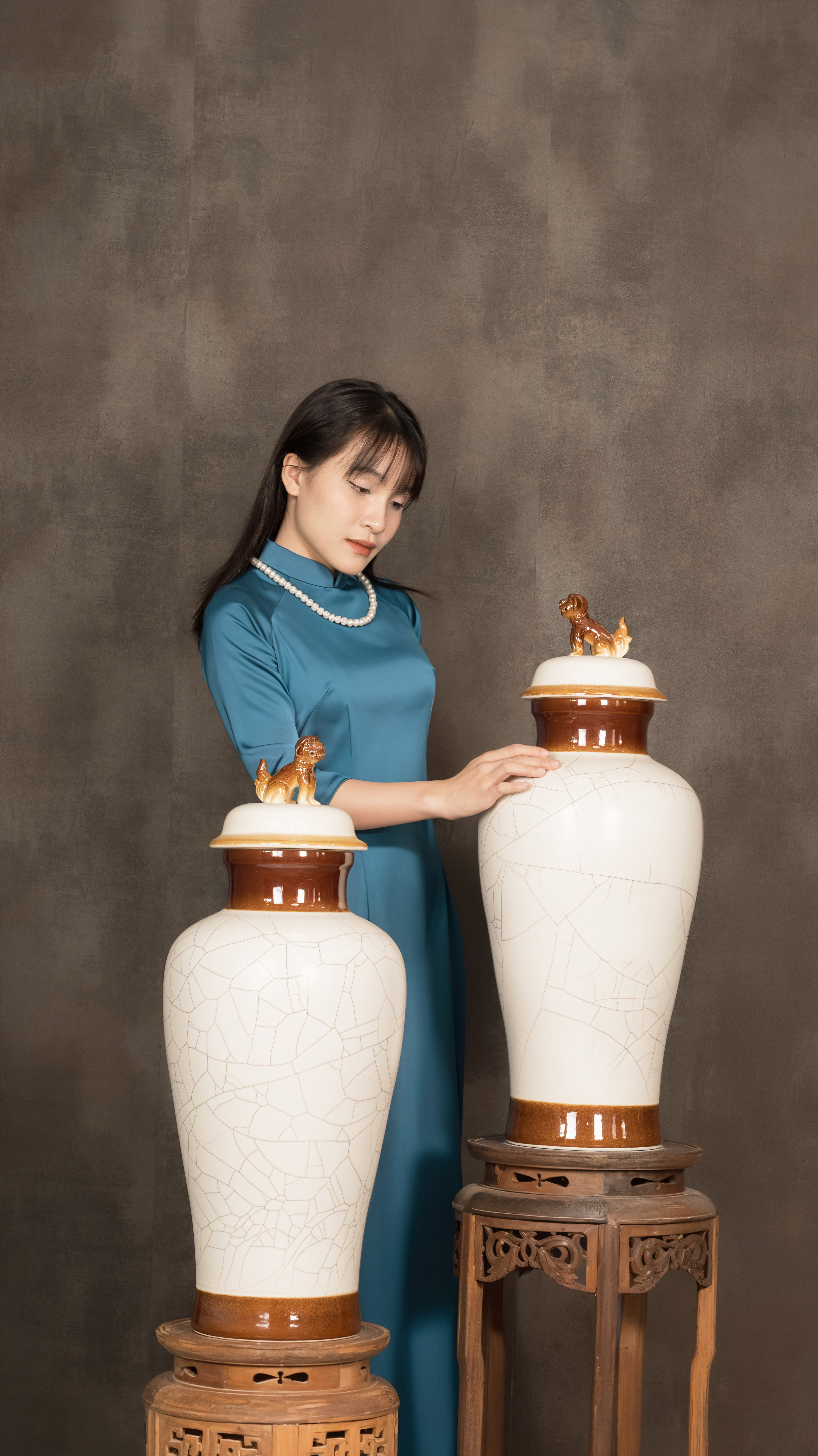 Woman in blue dress with large decorative vases in a studio setting.