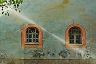 两个拱形格子窗位于一栋风化历史建筑的外墙上，散发着乡村魅力