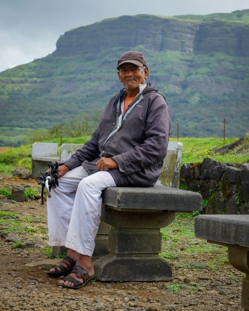 Free Senior man enjoying a peaceful moment in the rural Indian landscape with mountains in the background. Stock Photo
