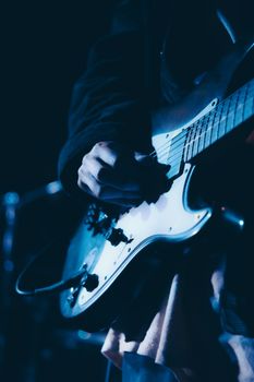 Dramatic close-up of a guitarist performing live on stage under blue lighting.