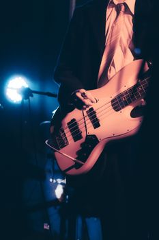 Close-up of a musician playing bass guitar in a live concert setting with blue stage lighting.