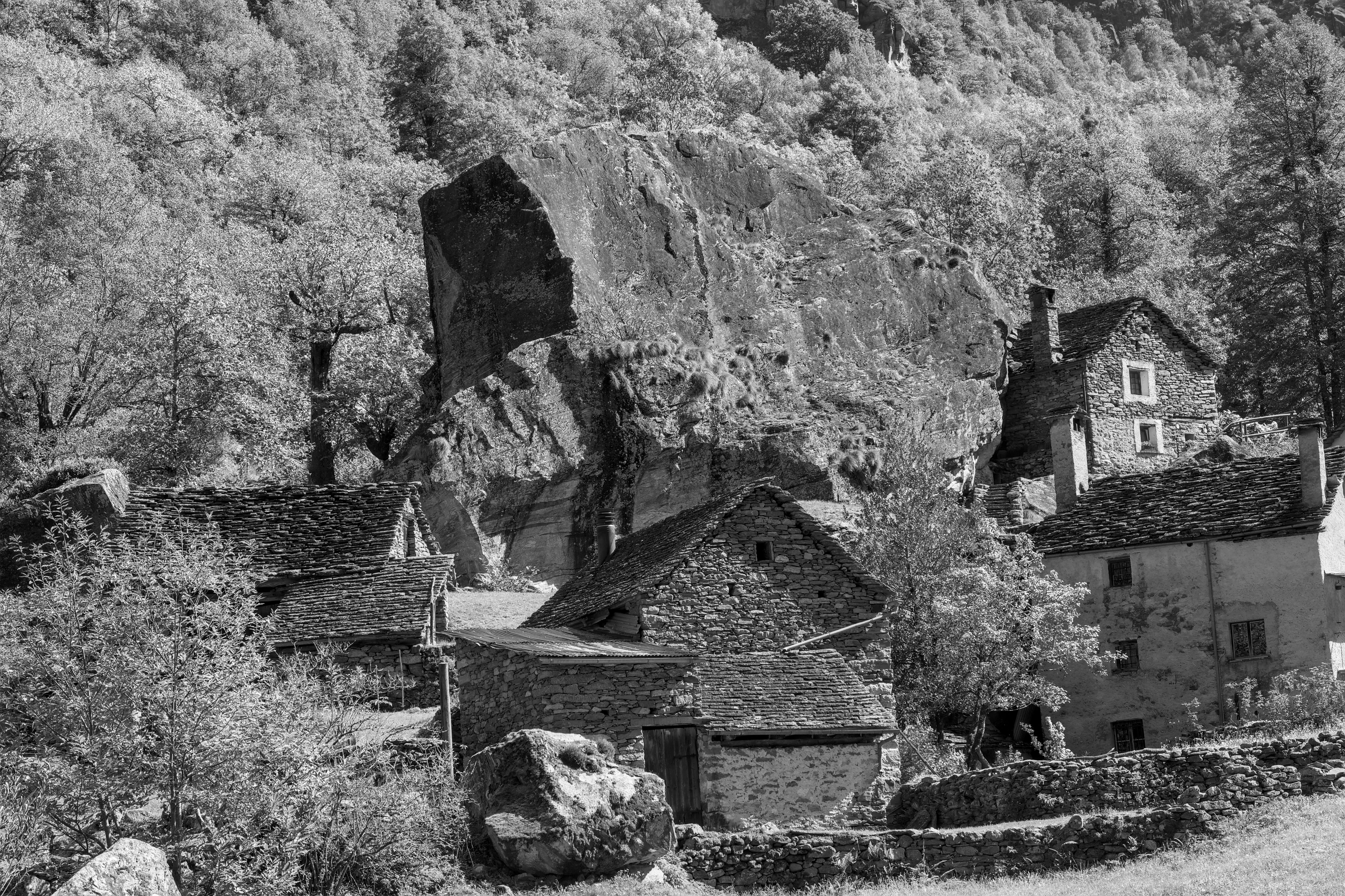 Black and white image of a rustic alpine village featuring traditional stone houses nestled against a rocky hill.