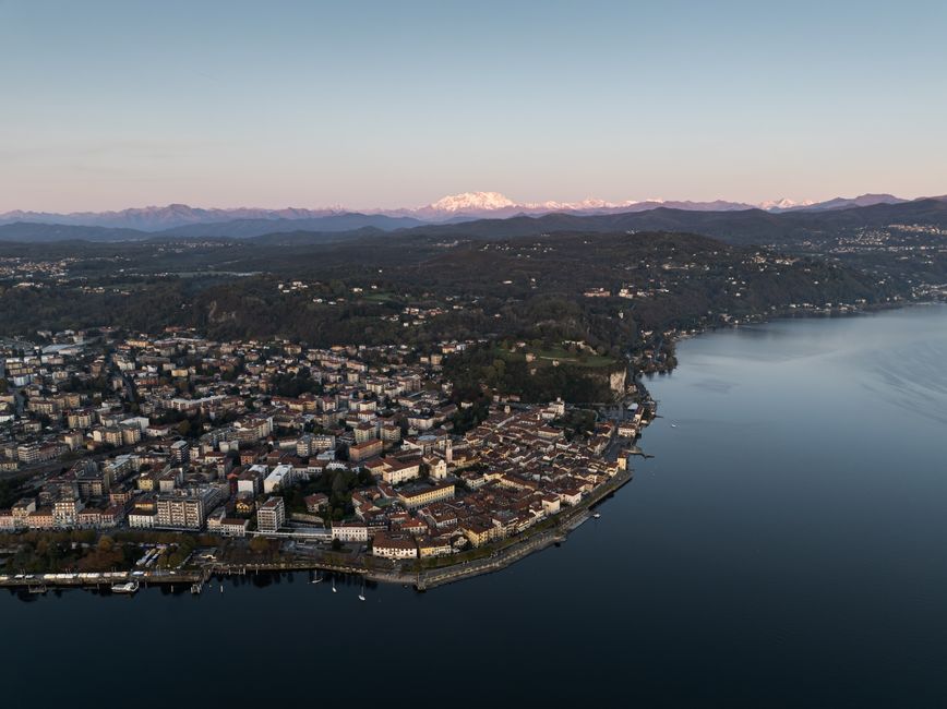 Unforgettable 30 Minutes Etna Volcano Private Helicopter Tour from Fiumefreddo Review Review 2026 - Aerial panorama of Arona, Italy by Lake Maggiore at dusk, with scenic mountains in the background.