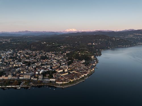 Free Aerial panorama of Arona, Italy by Lake Maggiore at dusk, with scenic mountains in the background. Stock Photo