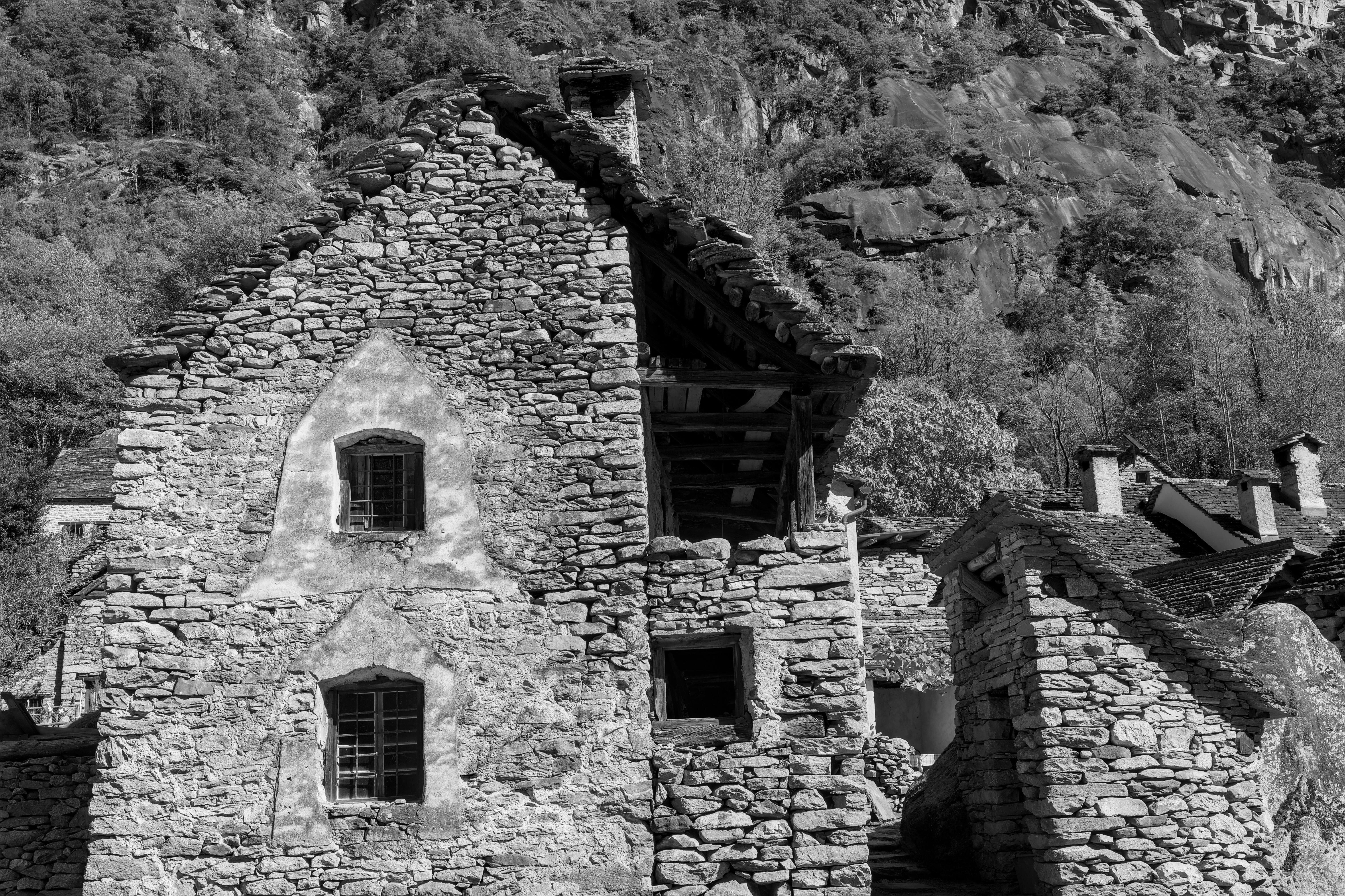 Black and white view of a rustic stone house nestled in Swiss mountains.