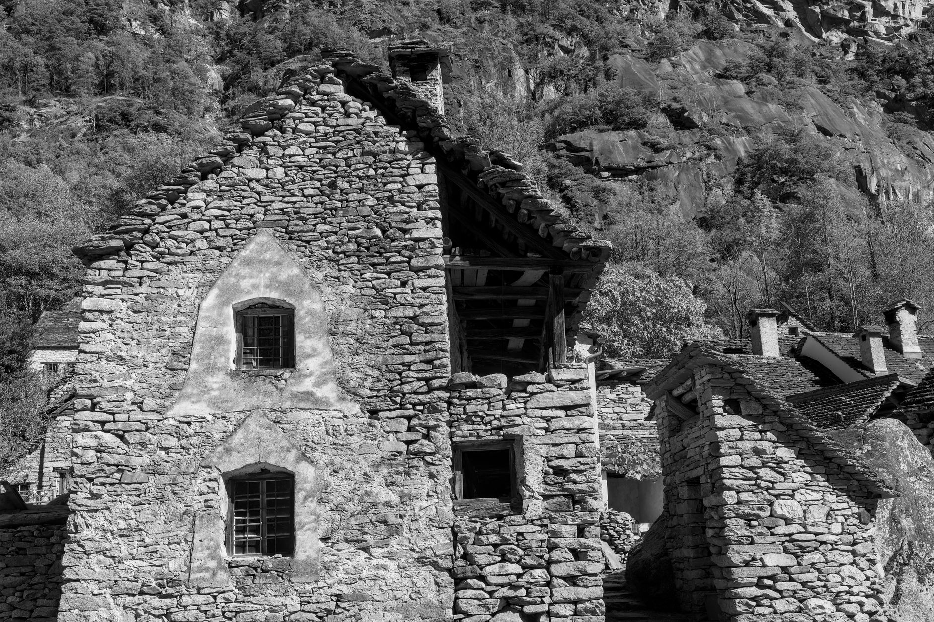 Black and white view of a rustic stone house nestled in Swiss mountains.