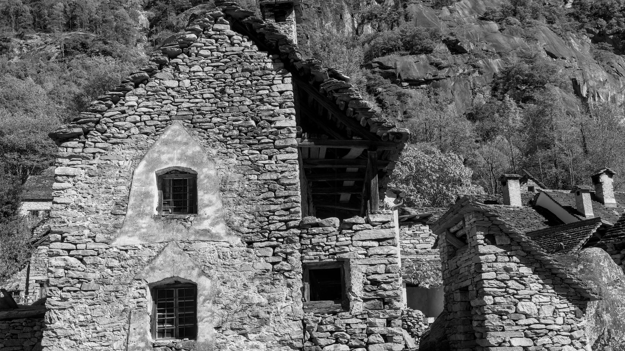 Black and white view of a rustic stone house nestled in Swiss mountains.