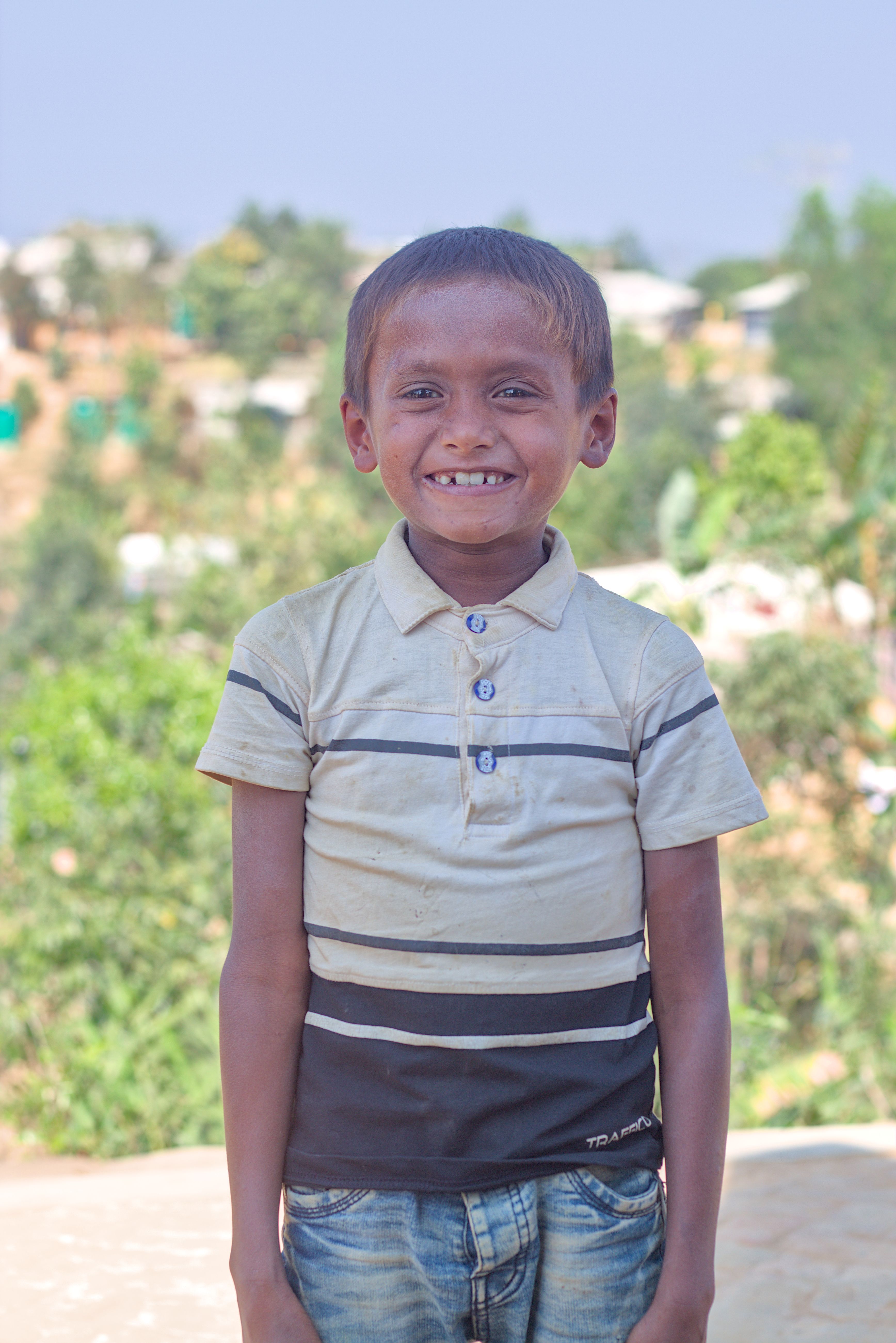 A smiling child stands outdoors with greenery in the background, conveying happiness and resilience.