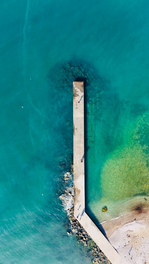Free Aerial shot of a pier extending into turquoise waters in Baniyas, Syria. Stock Photo