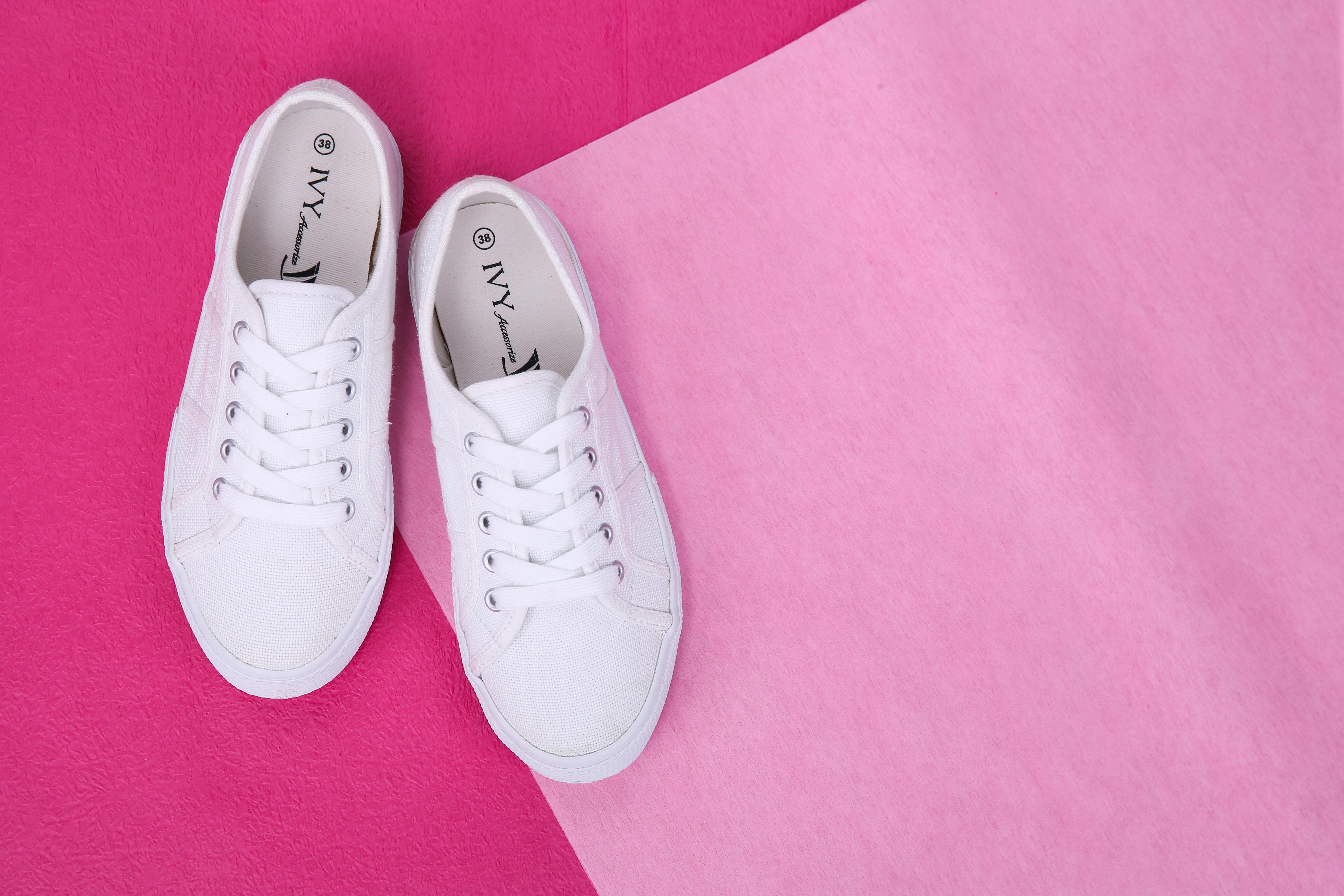 Flat lay of white sneakers with laces on a vibrant pink background, showcasing stylish footwear.