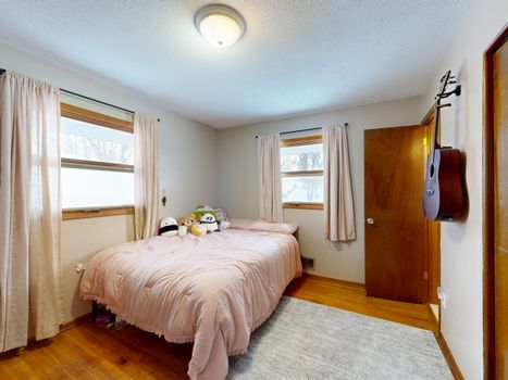 A warm bedroom with pink bedding, plush toys, and a guitar on the wall.
