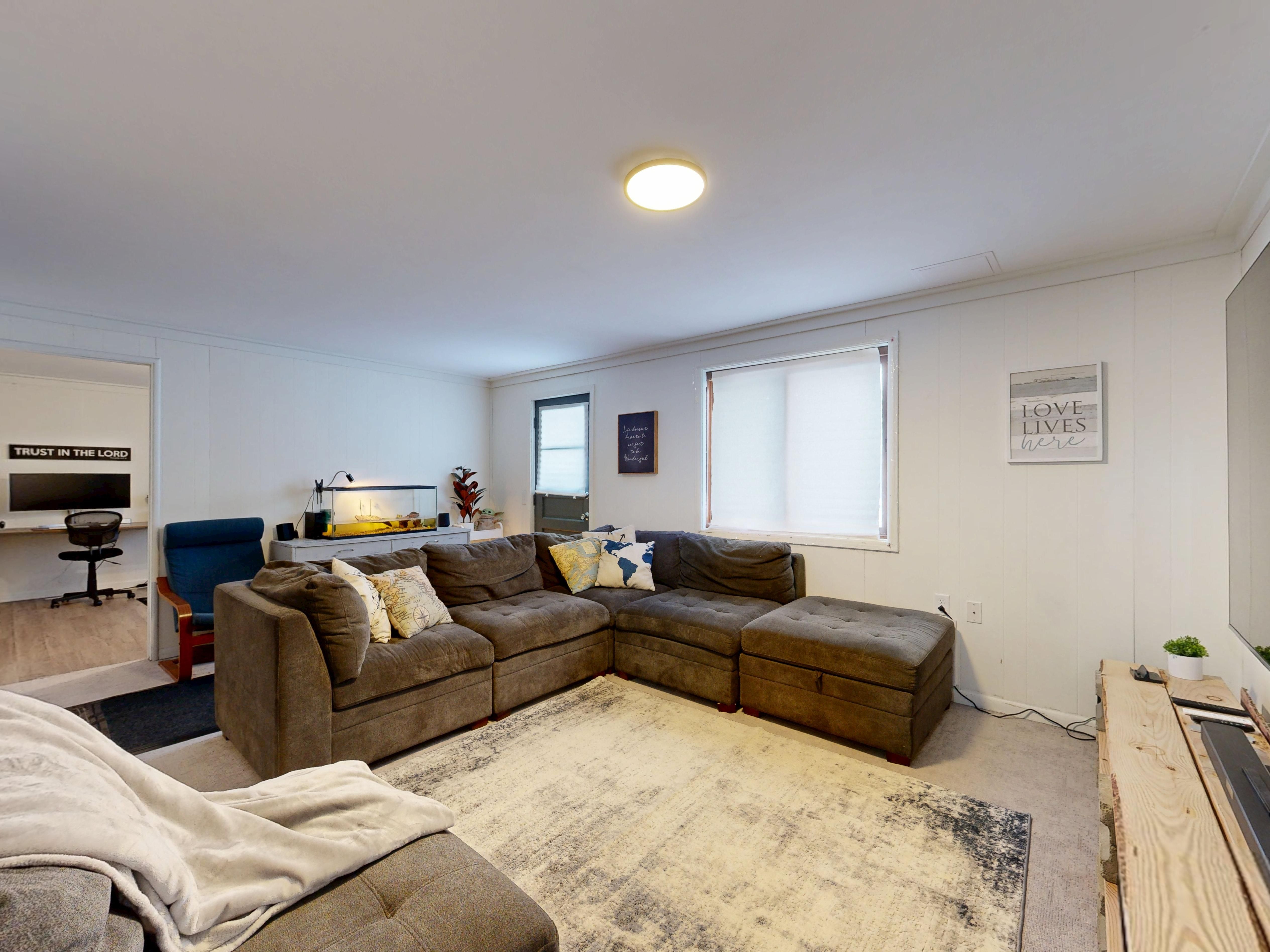 Sala contemporânea com sofá e uma estação de home office posicionada na lateral