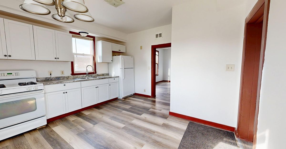 Spacious bright kitchen with white cabinets and wood flooring.