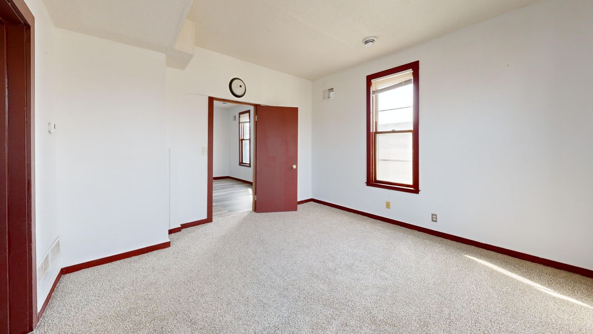 The reality behind a cozy Vermont listing: a bare room in beige carpet, white walls with red trim, one window, and a door standing open onto an unheated hallway, none of it resembling the staged photos.