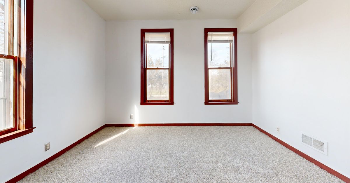 Spacious empty room with large red-trimmed windows and white walls, perfect for interior design.