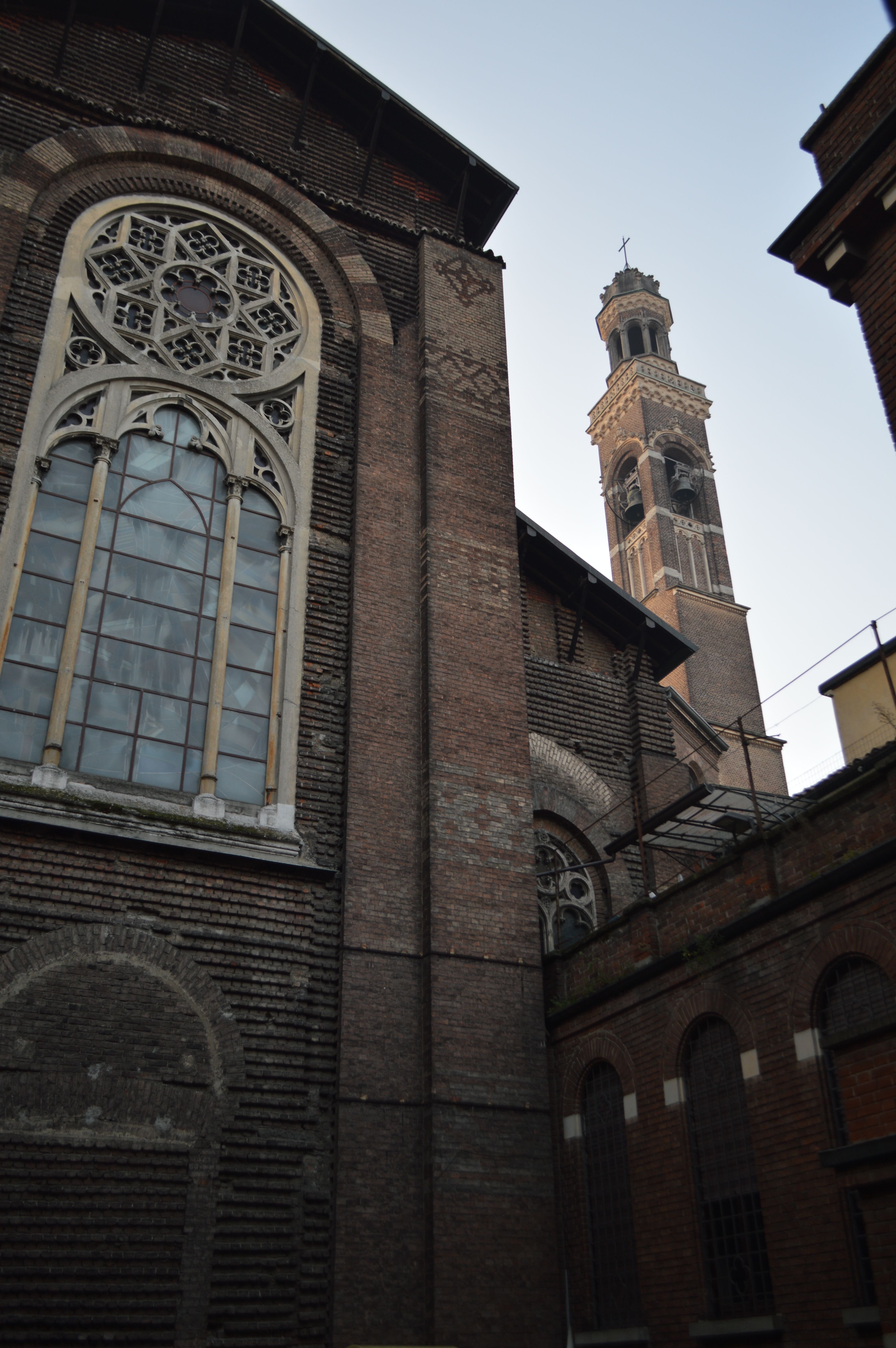 A detailed view of a historic brick church and tower with intricate windows at twilight.